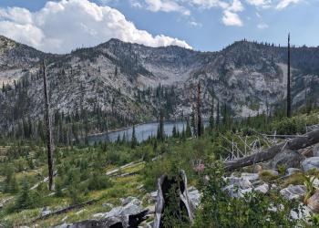 A high mountain lake surrounded by jagged mountains and burned trees.