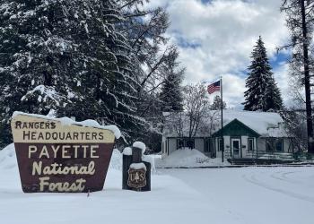 A white and green office building is pictured surrounded by trees and covered in snow.