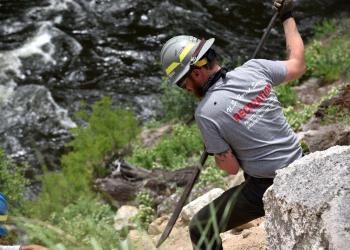 A person uses a tool to work on a trail along a river.