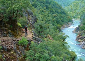 A biker on a trail with a river. 