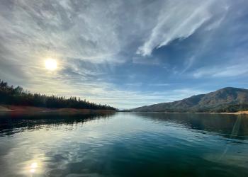 High clouds partially obscure the sun over mountains and a lake.
