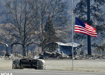 American flag flies in foreground, with burned building behind