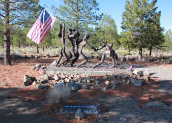 A photo of 4 metal sculptures of humans raising the American flag. 
