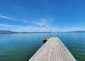 A boat dock on a clear blue lake with bright blue skies. A small fishing boat tied at end of dock. Eagle Lake, Lassen National Forest