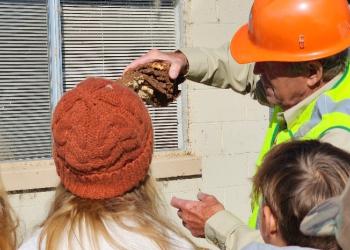Man holding up wood piece showing bark beetle damage to 6th grade students