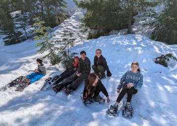 Students out on a snowshoe hike, sitting in snow in forest