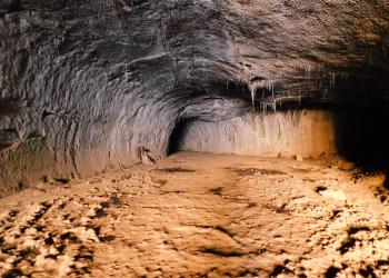 Inside of Subway cave lava tube in Hat Creek Ranger District. Icicles hanging from ceiling. Rocky dirt floor.