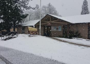 Hayfork Ranger Station is a light brown building and this image shows snow on the roof and grounds with the sidewalks shoveled.