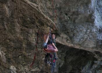 A volunteer in climbing gear with ropes and equipment hanging from the back of his harness scales the face of Natural Bridge to remove climbing anchors.