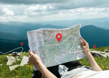 A person looking at a wilderness map while laying down on a mountain side. 