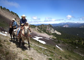 two men on horseback ride down a mountain trail