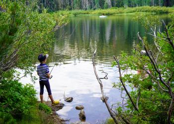 A kid fishing on the shore of a lake. 