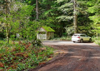 A car and restroom building in an unpaved parking area.