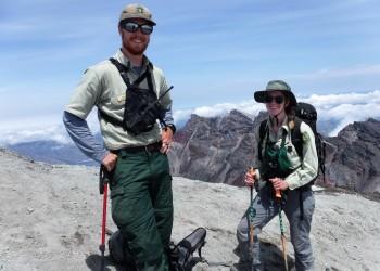 Two rangers stand on a mountain and smile at camera.