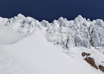 Climbers summiting a mountain surrounded by crags and snow.