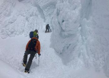 Several people climbing up a mountain, surrounded by snow and ice.