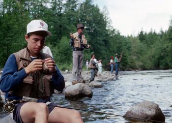 A group of people fishing on a river from the shore.