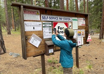 A person holding a cell phone scans a QR code for Scan and Pay on a poster at an information kiosk.