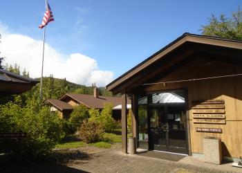 A wooden building on the right side of the screen with other buildings behind and a flag with red strips and white stripes can be seen flying on a pole. 