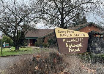 A sign that says "sweet home ranger station willamette national forest" in front of a wood building