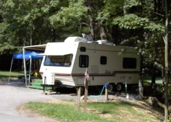 A white 25- foot long RV in a campsite with water and electricity hook ups. 