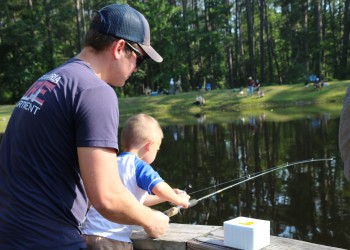 father helping little boy hold fishing pole