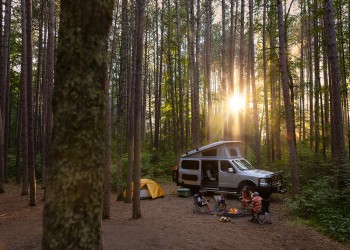 A van in a campsite with the sun in the background.