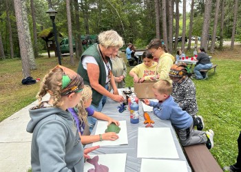 An educator surrounded by kids working on an art project.