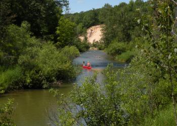 Two people canoeing in a red canoe in a river surrounded by the forest.