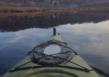 A point of view shot of a Kayak gliding along a mirror finished lake in fall. 