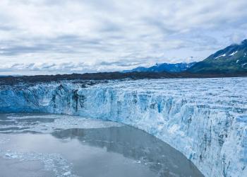 A bird's eye view of Childs Glacier during the summer. Cloudy sky with mountains in the background.