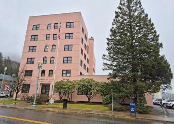 Pink building with windows, green shrubs along building, tall green tree to the right of the building