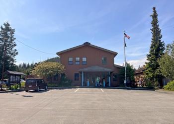 brown building, red car out front, parking lot, information kiosk, flag pole with American and state of Alaska flags flying
