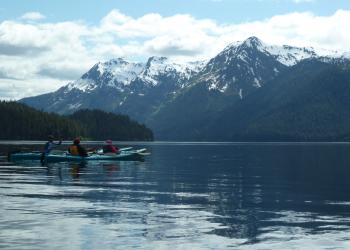 Kayakers approach a dramatic mountain area.