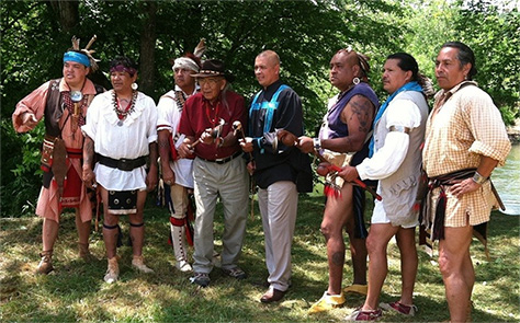 A group of Native American men wearing traditional garb pose for a photo before performing a traditional dance.