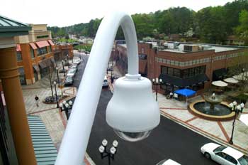 Image of a tall pole overlooking a business district.  A clear cyberdome houses a small video camera high above the street.