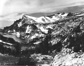 Photo of a forested snow covered mountain range with a lake next to it.