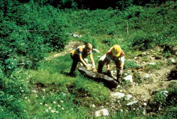 Photo of two workers placing a large flat rock onto a site.