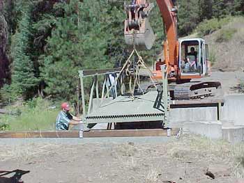 Photo of a track hoe placing a trail bridge on its abutments.