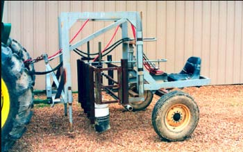 Photo of a sprayer hitched to a tractor. The sprayer is mounted on a steel frame with a seat for the operator that sits above two wheels.