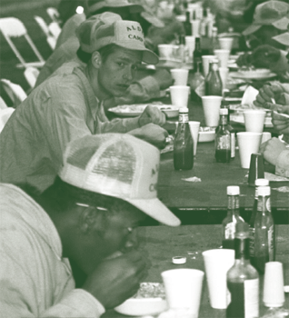 Photo of several people, all dressed similarly, eating in a cafeteria-style setting.