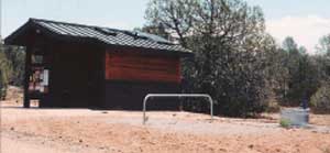 Photo of a hitch rail that is located near a bathroom and a horse trough.