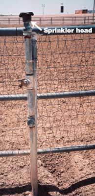 Photo of a sprinkler head on top of a fence rail at an outdoor arena.