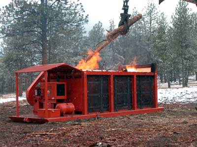 Photo of a Air Curtain Destructor that is being loaded with logs and other biomass fuels.