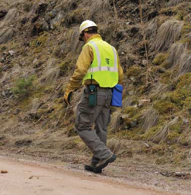 Photo of man working alongside a dirt road, he is wearing the ANSI/ISEA 207-2006 vest which allows easy access to the radio and other equipment on his waist belt. 
