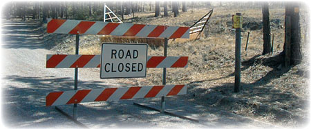 Photo of a road with a barricade that has a sign that reads, "ROAD CLOSED".