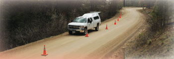 Photo of a Forest Service vehicle stopped along the side a roadway with cones setup along side the vehicle. 