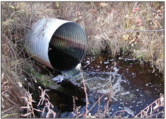 Image of an outlet pipe where a pool (scour hole) has formed at the base due to erosion.