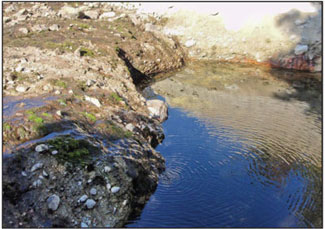 Image of where the side of a spillway has eroded and a pool has formed.