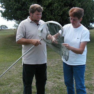 Picture of a man holding a net with a woman reaching for the captured monarch inside the net.